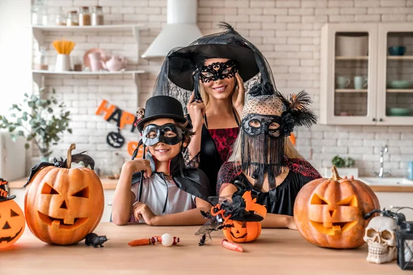 Concept d'Halloween. Mère et les enfants debout en costumes et masques dans la cuisine et en regardant la caméra — Photo