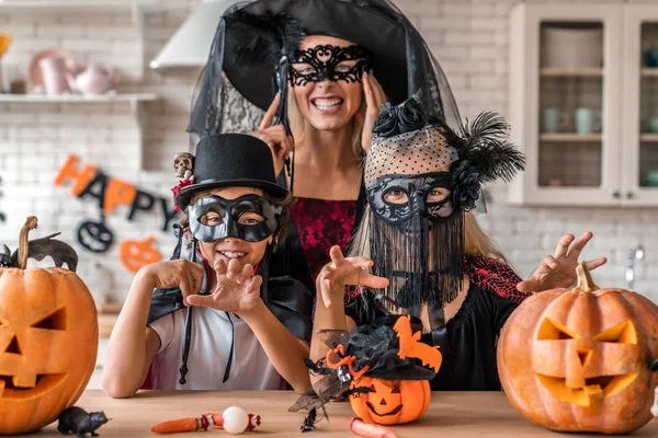 Conceito de Halloween. Mãe e crianças de pé em trajes e máscaras na cozinha e olhando para a câmera — Fotografia de Stock