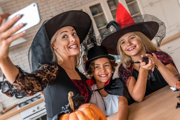 Jovem família feliz tirando selfie na cozinha decorada Halloween — Fotografia de Stock
