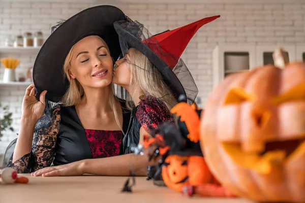 Klein schattig dochtertje zoenen haar moeder in kostuums op Halloween keuken — Stockfoto