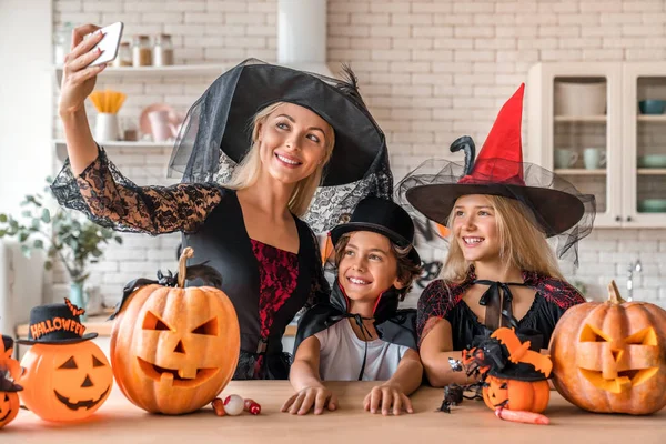 Sorrindo jovem mulher tomando selfie com seus filhos na cozinha decorada Halloween — Fotografia de Stock