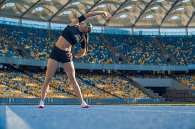 Koşucu koşmadan önce ellerini ve omuzlarını ısıtıyor. Koşu ve saha stadyumunda egzersiz yapan kadın sporcu..