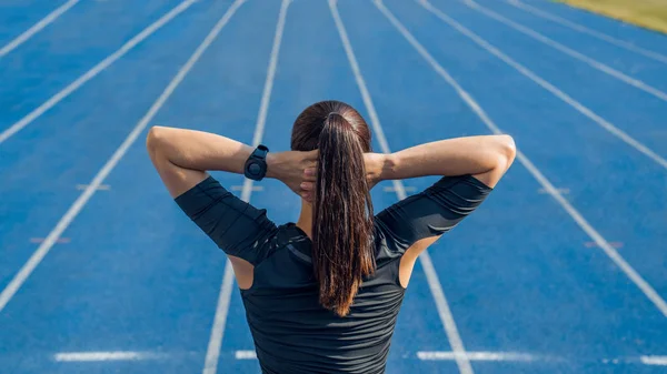 Rückansicht einer Läuferin, die sich vor einem Lauf mit Händen auf dem Kopf aufwärmt. Sportlerin macht Übungen im Leichtathletikstadion. — Stockfoto