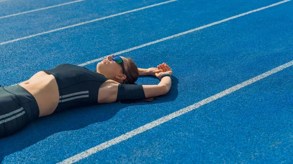 Woman athlete lying on the running track relaxing after workout. Female sprinter resting after workout lying on track on a sunny day. — Stock Photo, Image