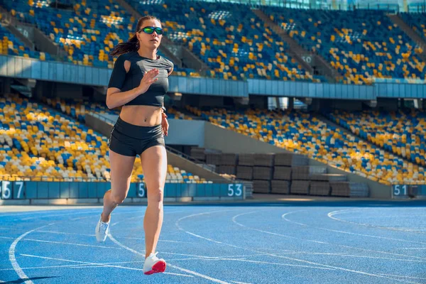 Female athlete sprinting on a running track in a stadium. — Stock Photo, Image