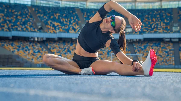 Young female sprinter runner stretching legs on stadium track — Stock Photo, Image