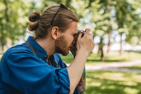Молодой человек в повседневной одежде фотографирует пейзаж, стоя в городском парке на открытом воздухе — стоковое фото