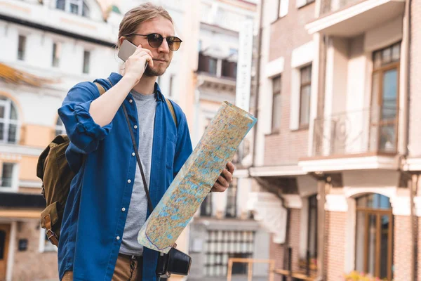 Schöner junger Mann in lässiger Kleidung, der im Freien telefoniert und eine Karte in der Hand hält — Stockfoto