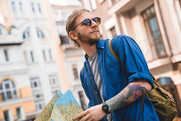 Nahaufnahme eines gutaussehenden jungen Mannes in lässiger Kleidung, der eine Karte in der Hand hält und im Freien wegschaut — Stockfoto