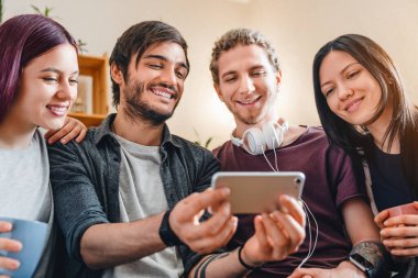 Neşeli çok ırklı arkadaş grubu evde dinlenirken akıllı telefondan program izliyor.