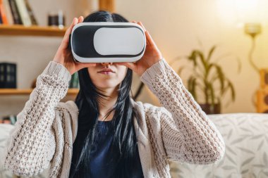 Kanepede otururken VR kulaklık takan genç bir kadın.