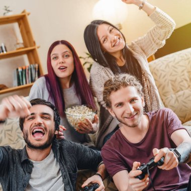 Video oyunu oynayan ve evde kutlama yapan bir grup genç arkadaş.