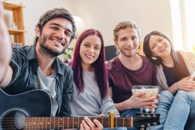 Evdeki kanepede rahat rahat oturup, gitarla selfie çeken arkadaşlar.