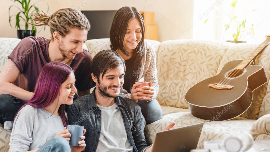 Happy group of friends laughing together with laptop sitting on sofa at home