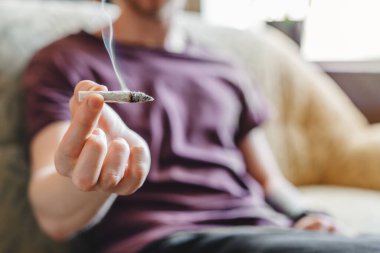 Cropped image of young man smoking marijuana or cigarette indoors clipart