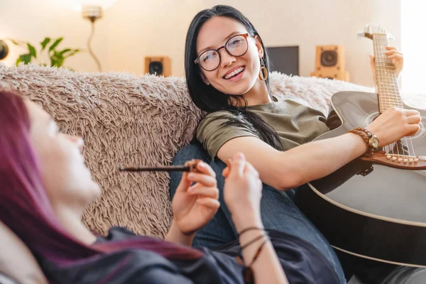 Sonriente Chica Jugando Guitarra Mientras Novia Fumando Pipa Interior —  Fotos de Stock