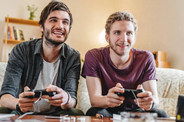 Dua Pemuda Tersenyum Bermain Video Game Sambil Duduk Sofa Rumah — Stok Foto