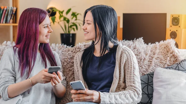 Dos Amigas Sonrientes Ropa Casual Con Teléfonos Móviles Sentadas Sofá —  Fotos de Stock