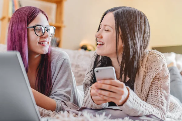 Two beautiful young women relaxing on the living room floor with laptop computer and looking on each other