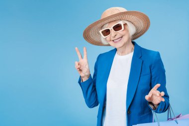 Mavi arka planda torbalarla alışveriş yapan olgun bir kadın.