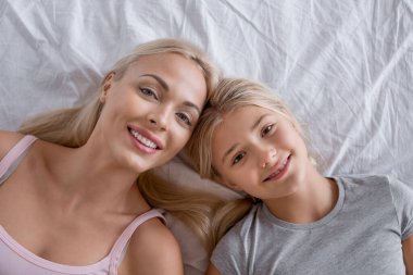 Mutlu anne ve kızının yatakta yatışının üst görüntüsünü kapat..