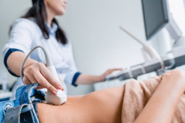Close up of female doctor doing ultrasound probe on patient stomach in medical clinic clipart