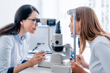 Yetişkin kadın doktor göz doktoru modern klinikte genç bir kızın gözlerini kontrol ediyor.