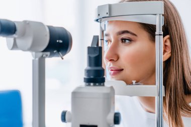 Modern oftalmoloji kliniğinde güzel bir genç kız göz görüşünü kontrol ediyor.