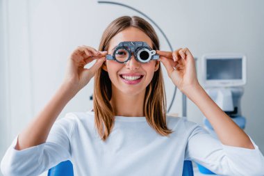 Göz muayenesi sırasında göz testi gözlükleriyle görüşü kontrol eden genç bir kadın.