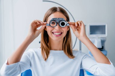 Young woman checking vision with eye test glasses during a medical examination at the ophthalmological office clipart