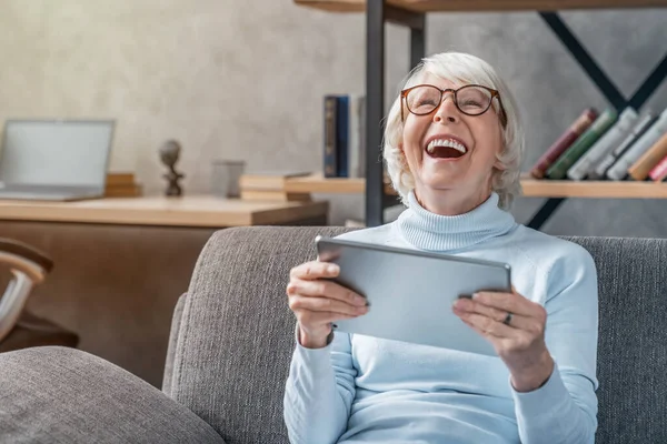 Mulher Sênior Feliz Olhando Rindo Seu Tablet Digital Sofá — Fotografia de Stock