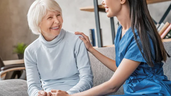 Friendly asian assistant caring senior woman home in living room