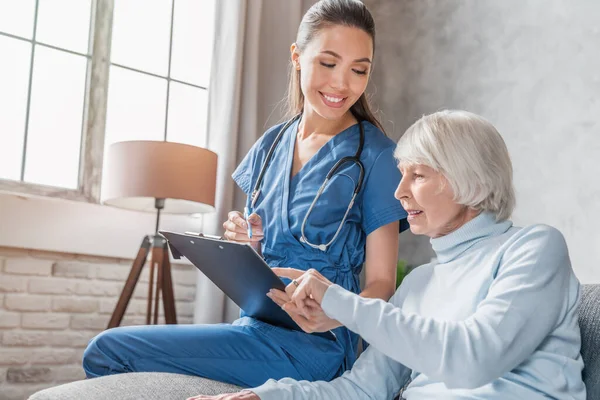 Lächelnde Seniorin Liest Medizinische Tests Und Bekommt Besuch Von Krankenschwester — Stockfoto