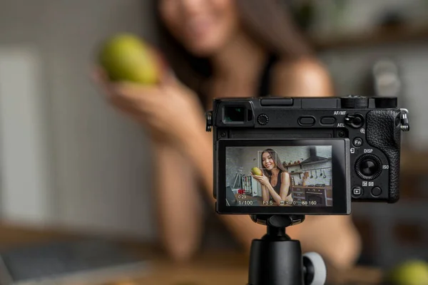 Young female blogger on camera screen holding mango for healthy eating vlog