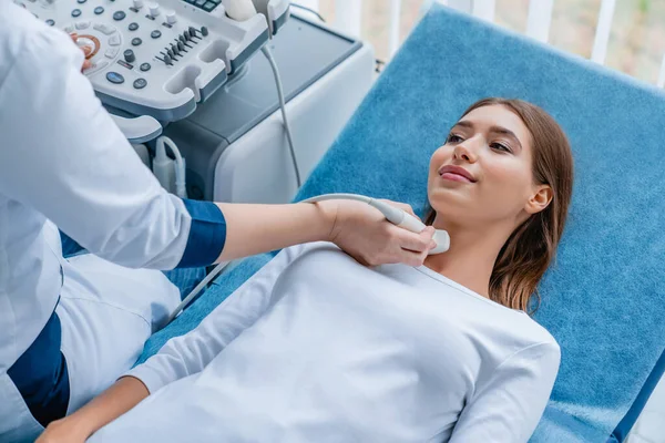 Modern klinikteki doktoru tarafından boyun ultrason taraması yaptıran genç bir kadın.