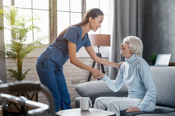 Happy Female Professional Caregiver Taking Care Elderly Woman Home Stock Photo