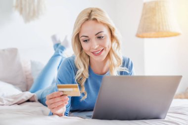 Mutlu kadın evden bilgisayarla online alışveriş yapmak için kredi kartını kullanıyor.