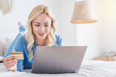 Evden bilgisayarla online alışveriş yapmak için kredi kartını kullanan mutlu bir kadının portresi