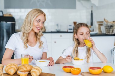 Anne ve kızı kahvaltıda portakal suyu içiyor.