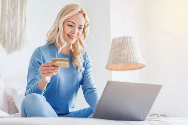 女人坐在床上用笔记本电脑和信用卡上网购物 — 图库照片