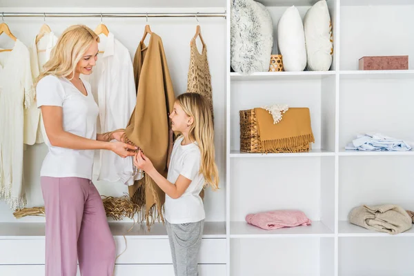 Mother choosing clothes to her girl daughter from wardrobe at home