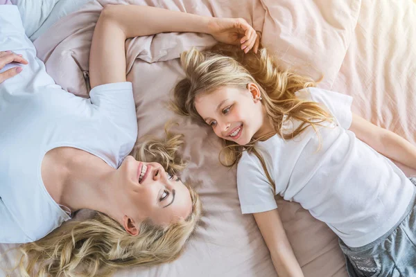 Top view of happy mother with her daughter lying in bed in the morning at home