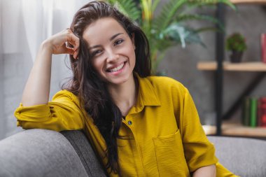 Evdeki kanepede oturan rahat, gülümseyen kadın. Ev hayatı kavramı