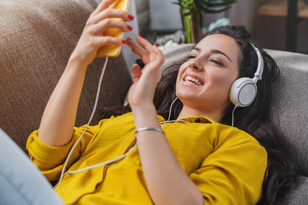Wanita Muda Yang Bahagia Berbaring Sofa Dengan Smartphone Dan Headphone — Stok Foto