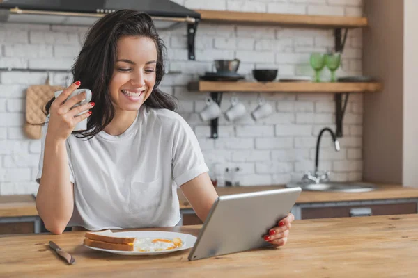 在现代厨房用数码平板电脑享用健康早餐的年轻漂亮女人 — 图库照片