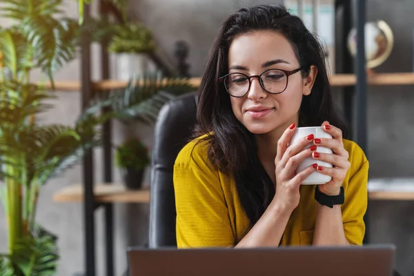年轻美丽的微笑的女人在家里的小办公室里一边工作一边在笔记本电脑上学习 一边喝着咖啡 — 图库照片