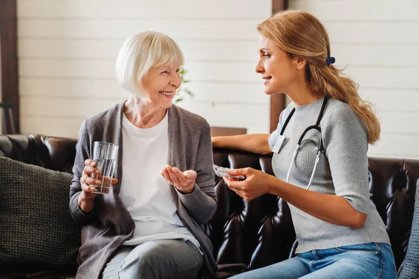 Glimlachende Verpleegkundige Geeft Glas Water Medicijnen Aan Senior Patiënt — Stockfoto