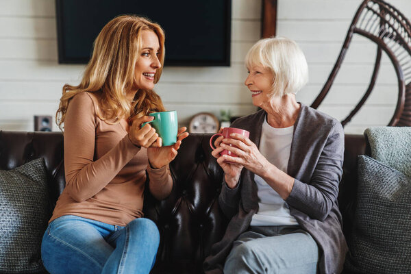 Smiling Mature Mother Adult Daughter Sofa Living Room Talking Drinking Stock Picture