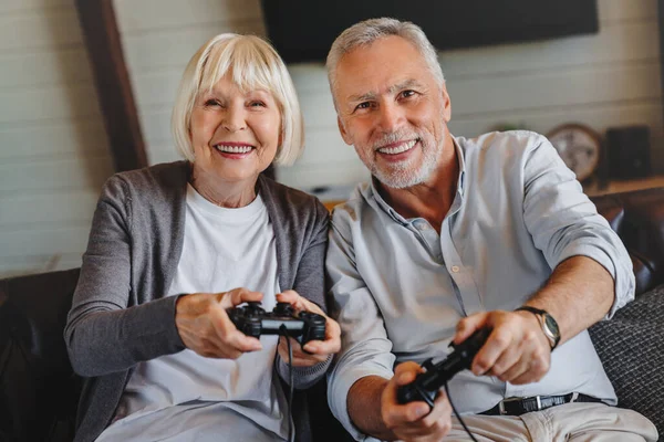Pasangan Senior Yang Bahagia Duduk Bersama Sofa Memegang Kontroler Saat — Stok Foto