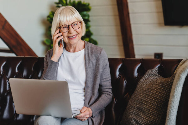 Mature Woman Talking Mobile Phone While Using Laptop Living Room Stock Photo